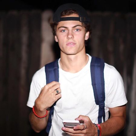 Harry Raftus giving a pose to a picture while using his phone and carrying a bag